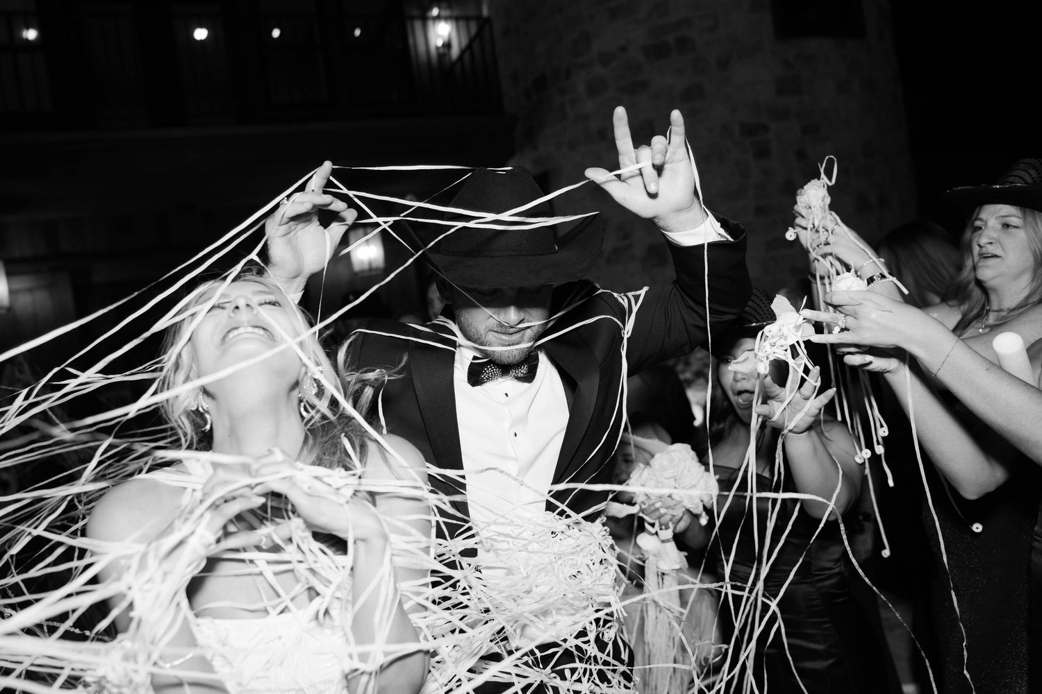 Celebratory scene with streamers and confetti raining down on formally dressed people at a nighttime party celebration.