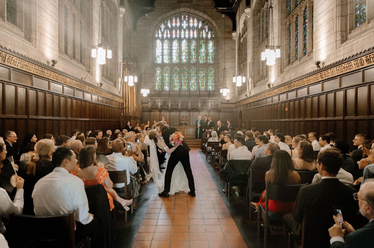 Church goers seated in wooden pews during a service in a grand gothic cathedral with soaring stone arches and stained glass.