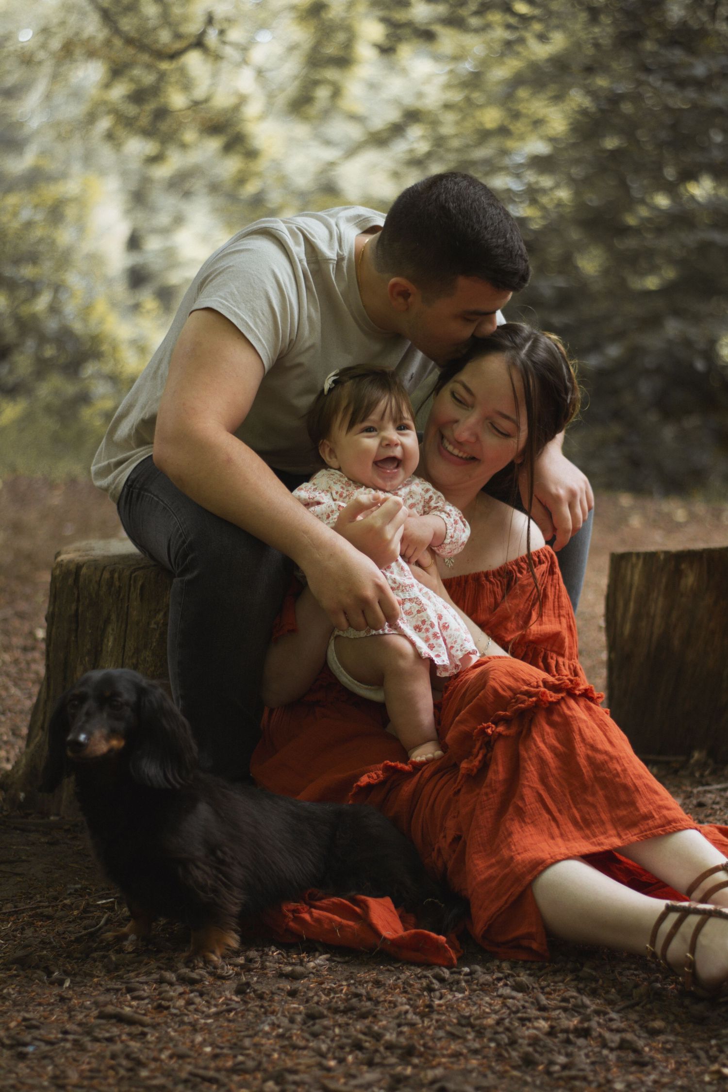 A happy family moment in the woods with their black dog as they play and laugh together.