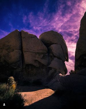 Dramatic purple sunset sky over large boulder formations in Joshua Tree National Park.