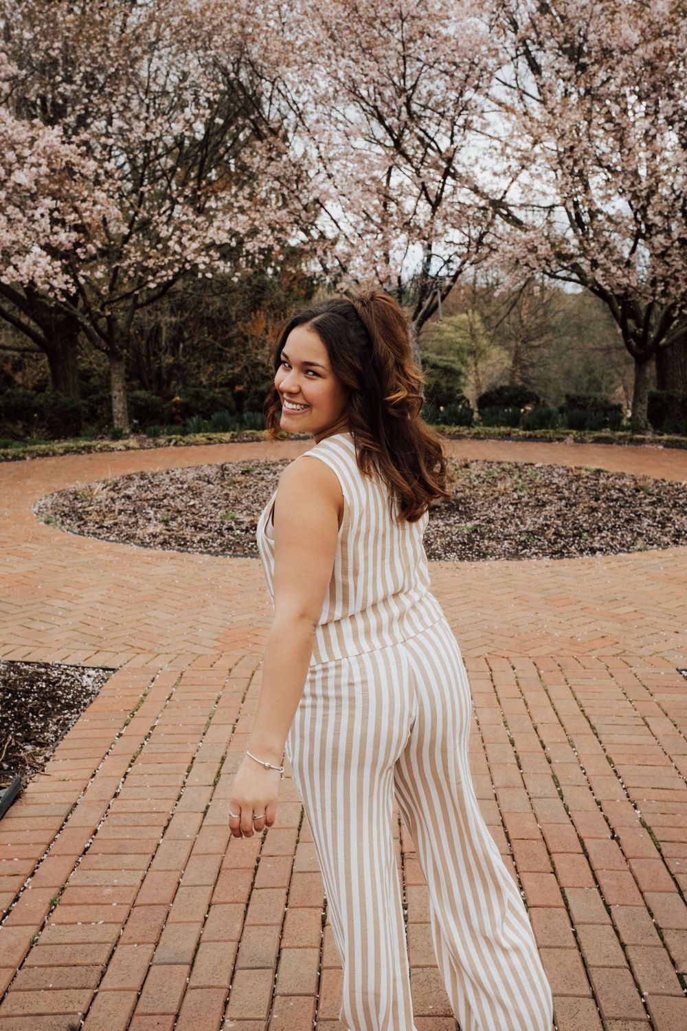 A sequence of photos showing a joyful graduate twirling in a striped jumpsuit under blooming cherry trees at Hershey Gardens.
