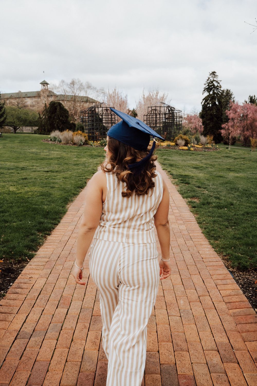 A high school senior walks with graduation cap for senior photoshoot at Hershey Gardens.