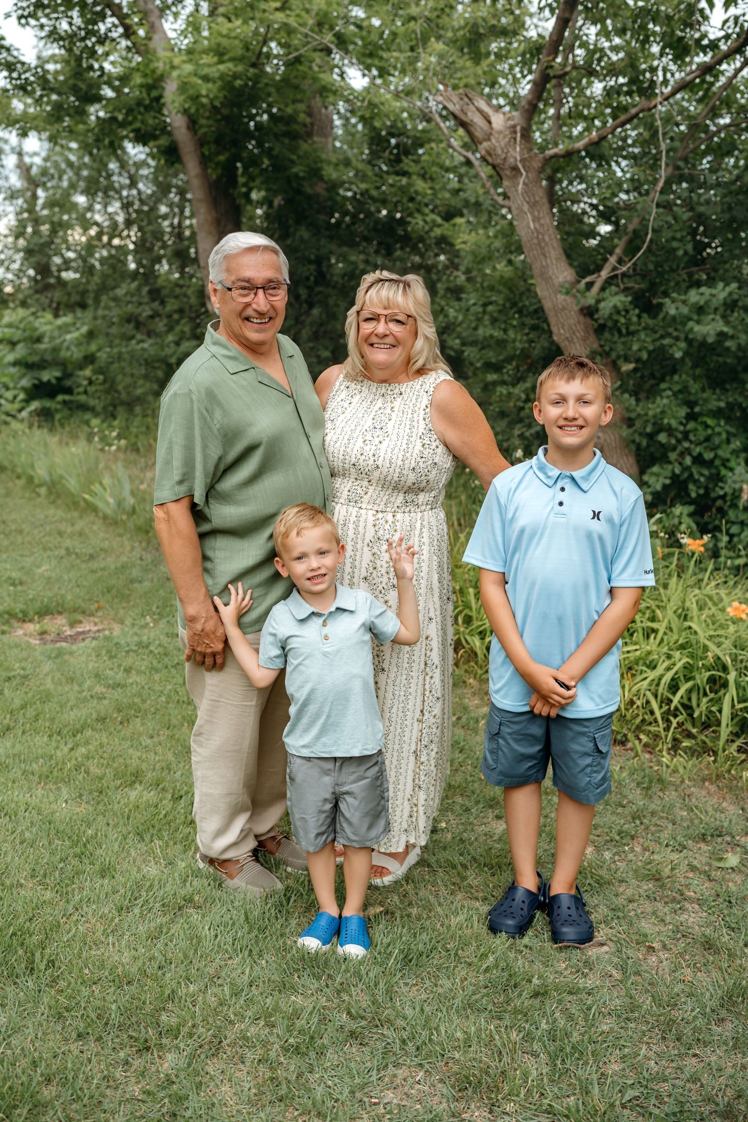 Family group posing together outdoors on grassy lawn with green trees in background.
