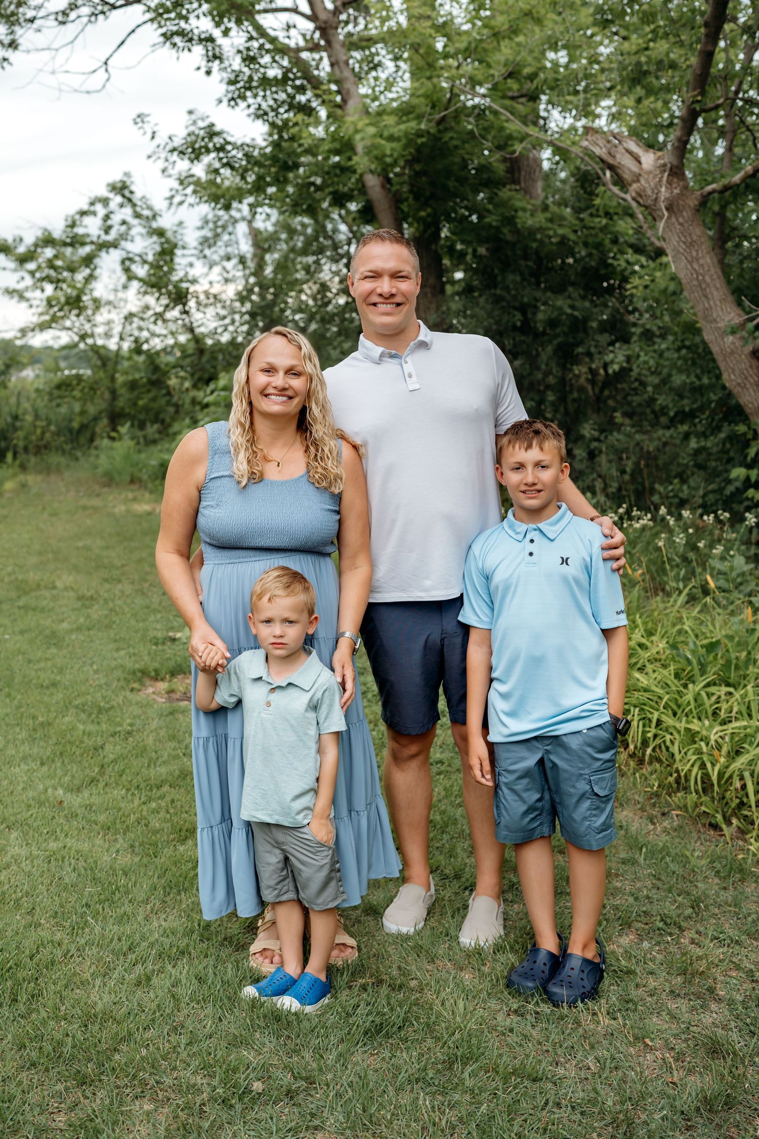 Family wearing coordinating blue outfits poses together for outdoor portrait in a garden setting.