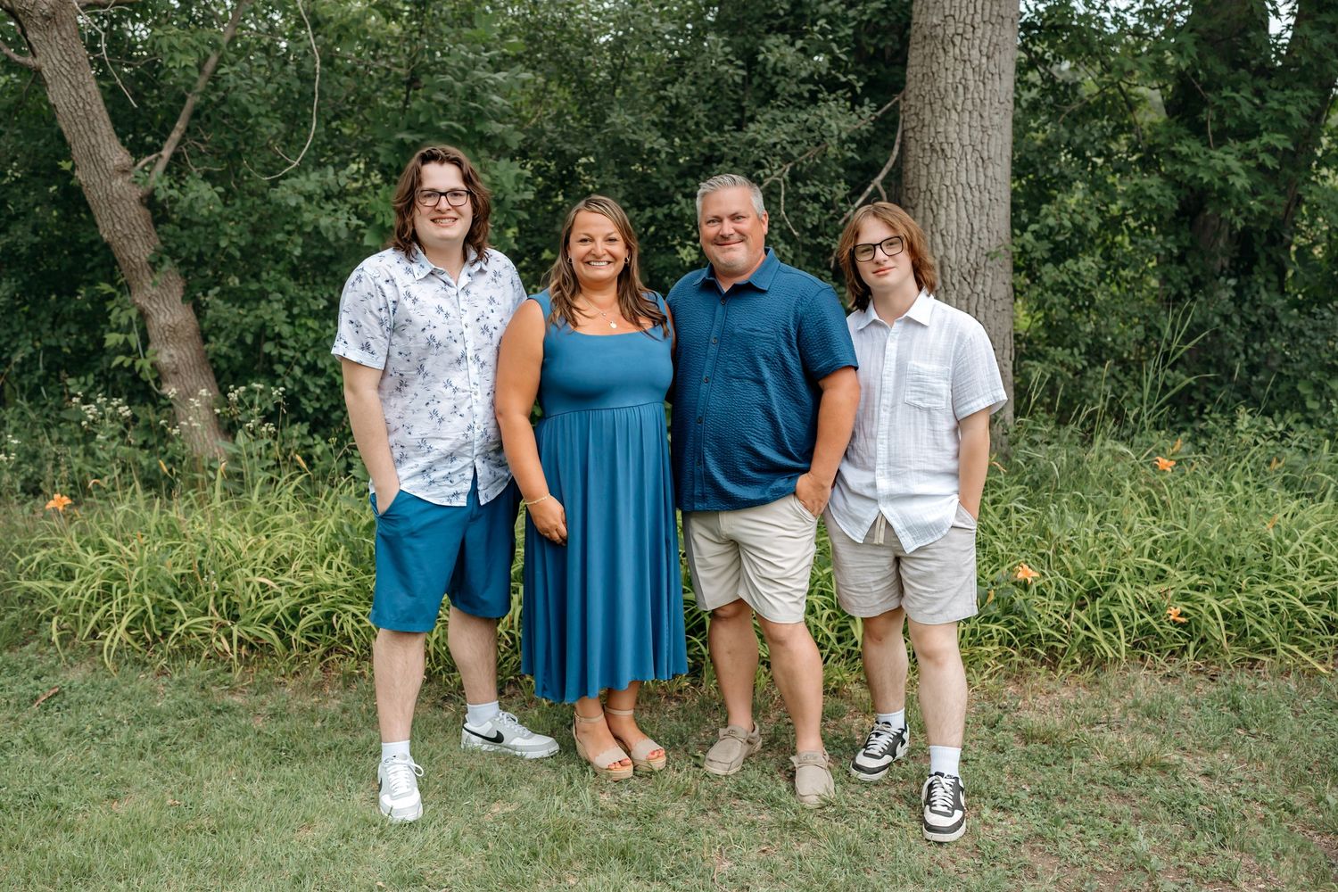 A group photo shoot in a lush green outdoor setting showcasing casual summer outfits and natural poses.