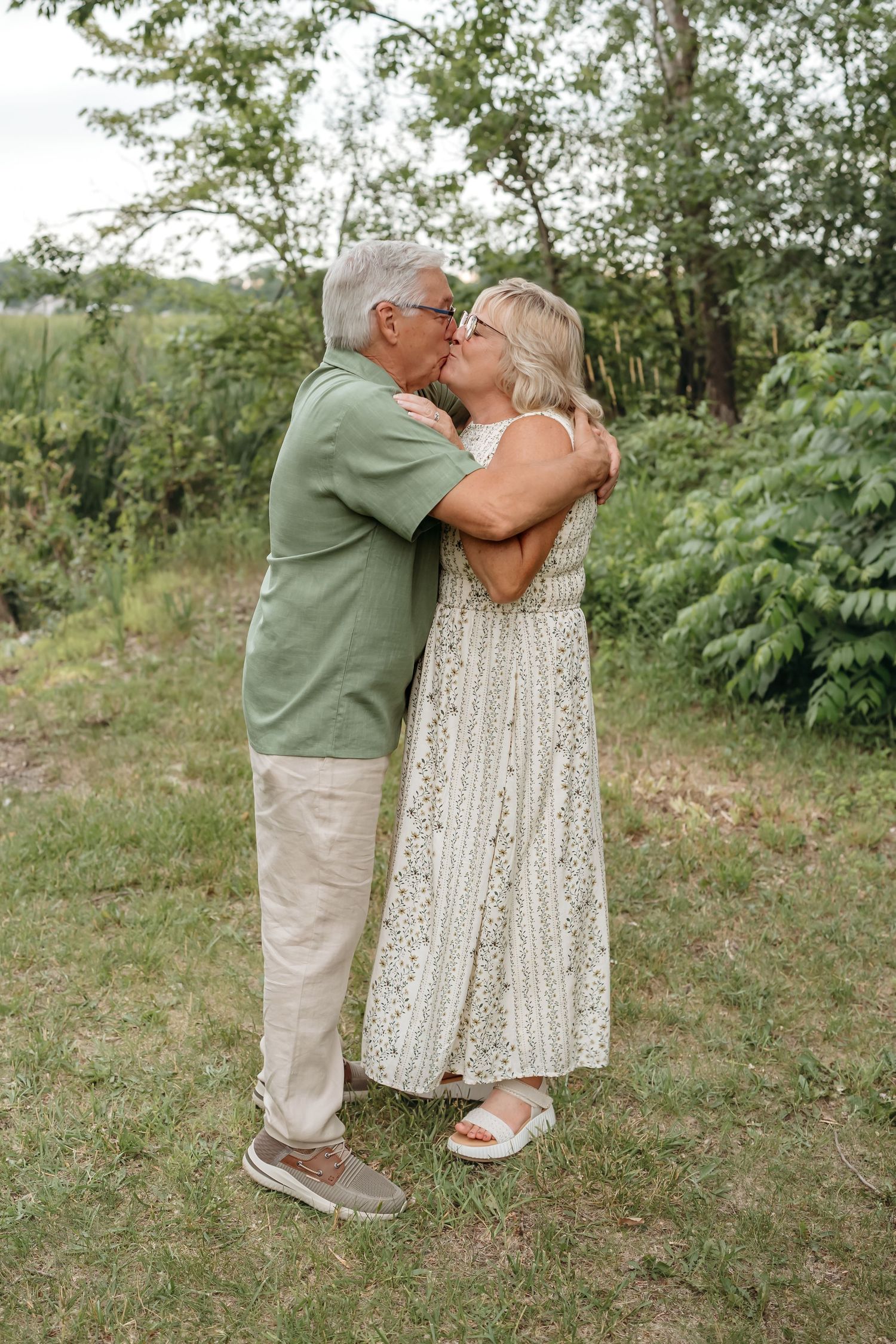 Seniors holding hands lovingly while standing together on grassy hillside.