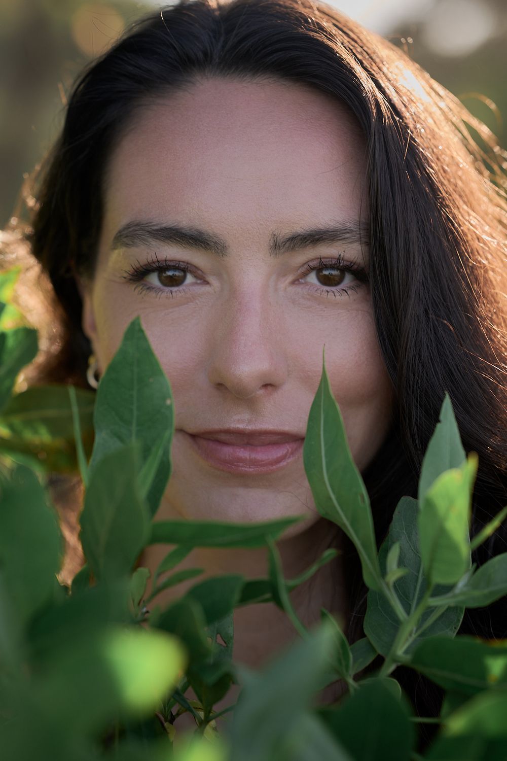 Close up portrait framed by green leaves in natural outdoor setting.