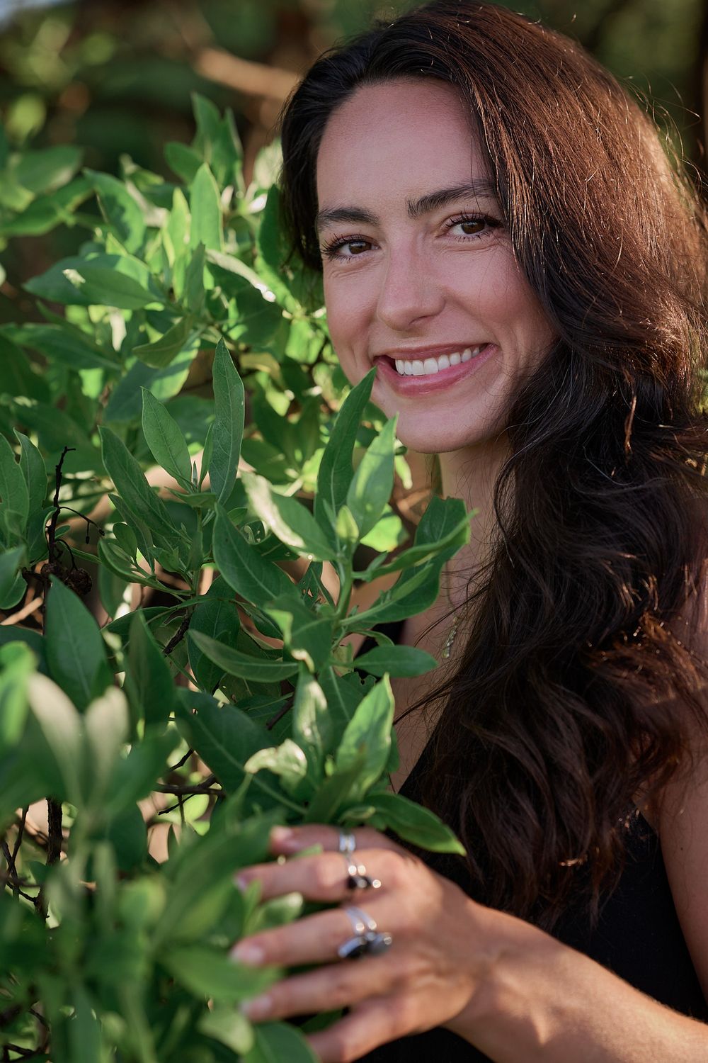 Outdoor portrait series with dark curly hair and green foliage in the background.