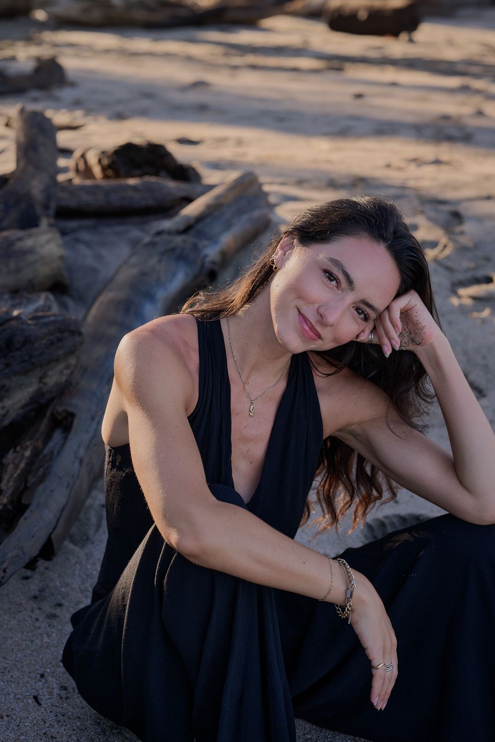 A woman in a black dress poses on a beach at sunset, creating a moody and artistic outdoor portrait.