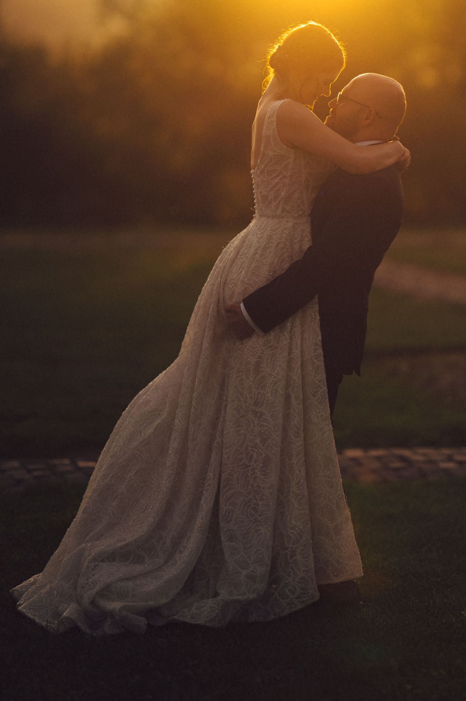 A couple embraces in a romantic moment at sunset with the bride wearing a flowing white lace wedding dress.