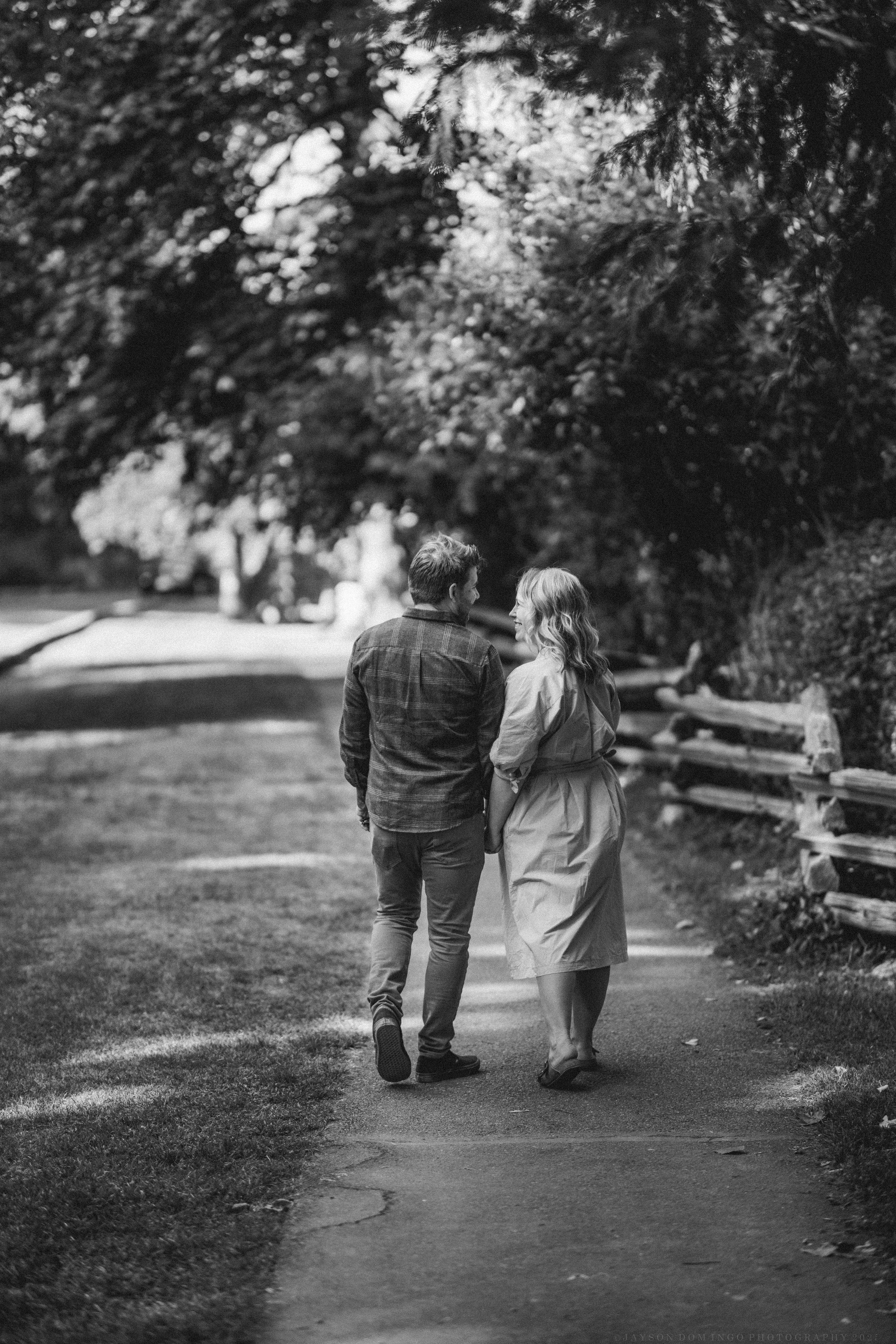 A couple takes a romantic stroll together along a tree-lined path in black and white.