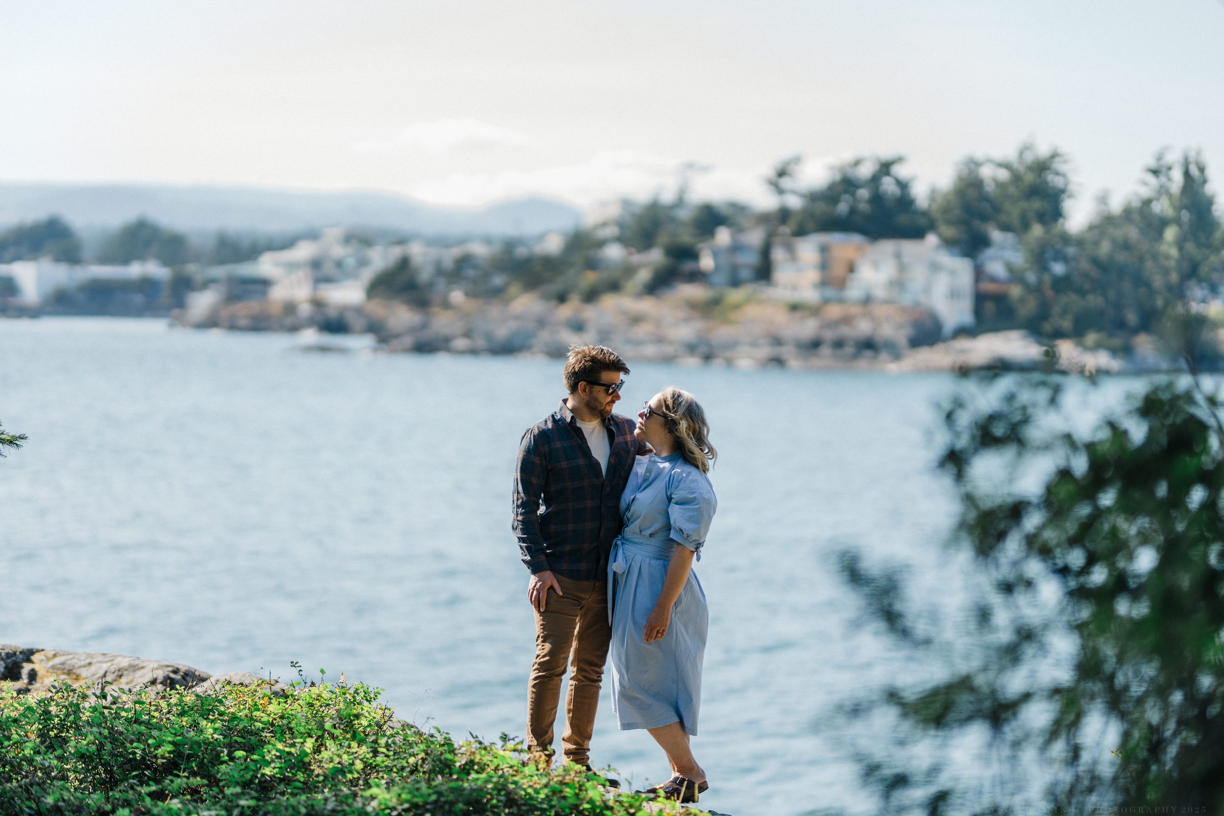 Couple embraces while enjoying scenic coastal views along waterfront path with city in background.