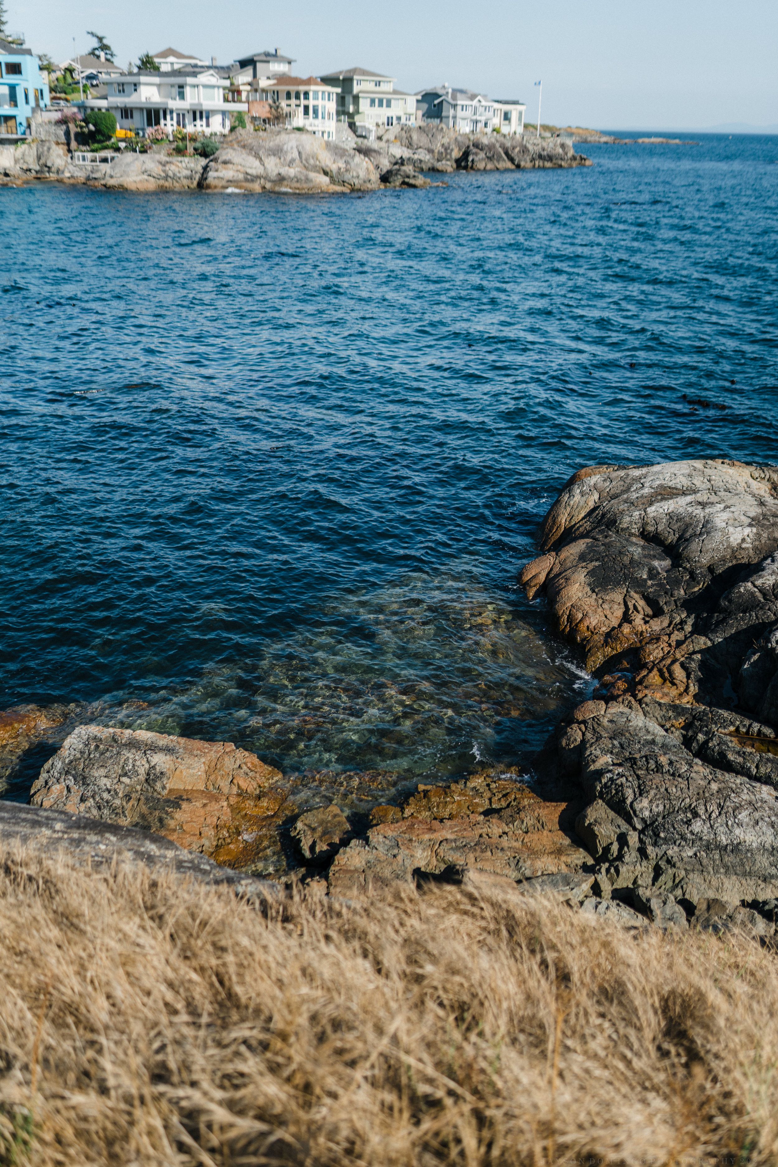 Coastal homes perched on rocky cliffs overlooking deep blue waters with rugged shoreline in the foreground.