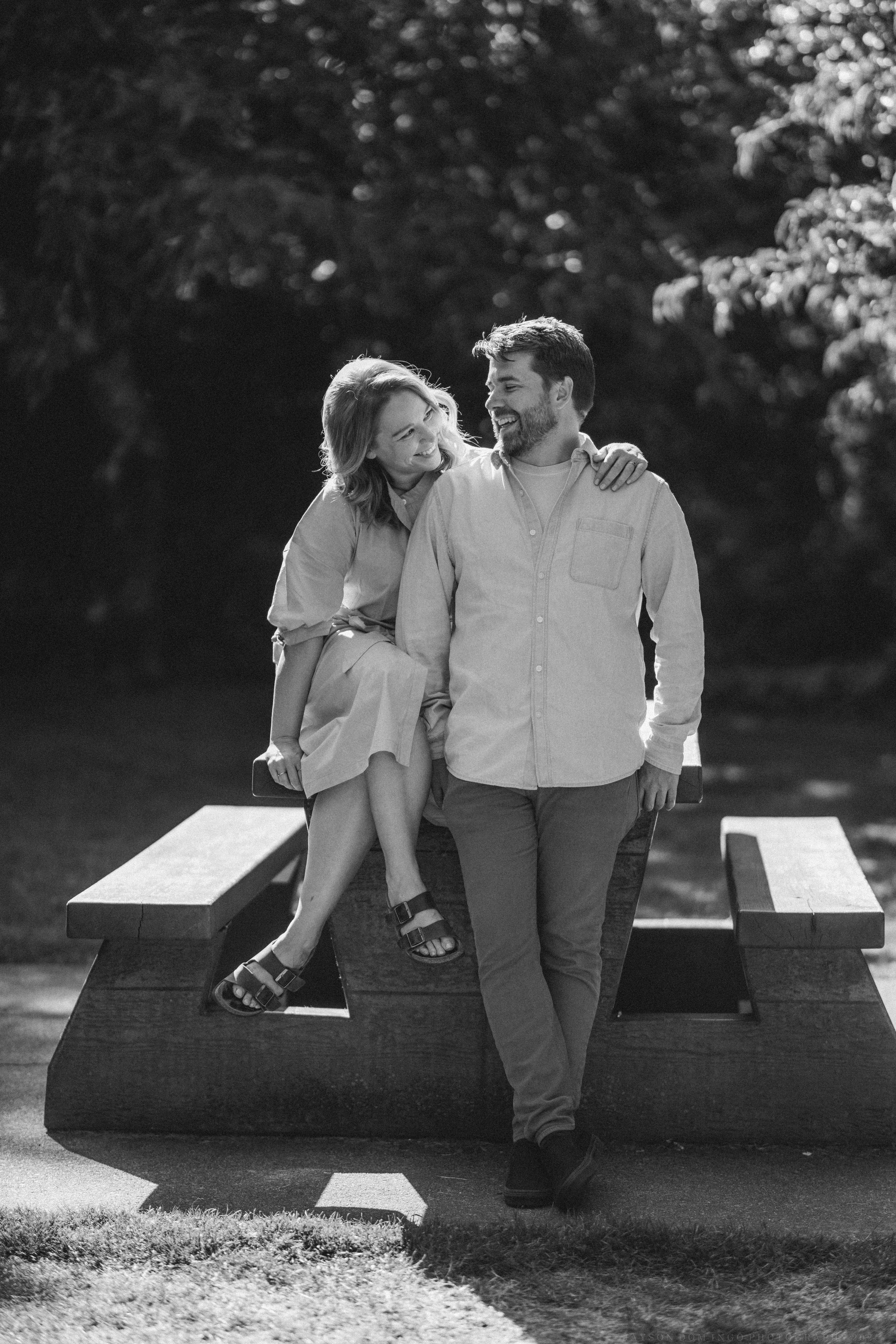 Couple sitting close together on wooden benches in a black and white outdoor scene.
