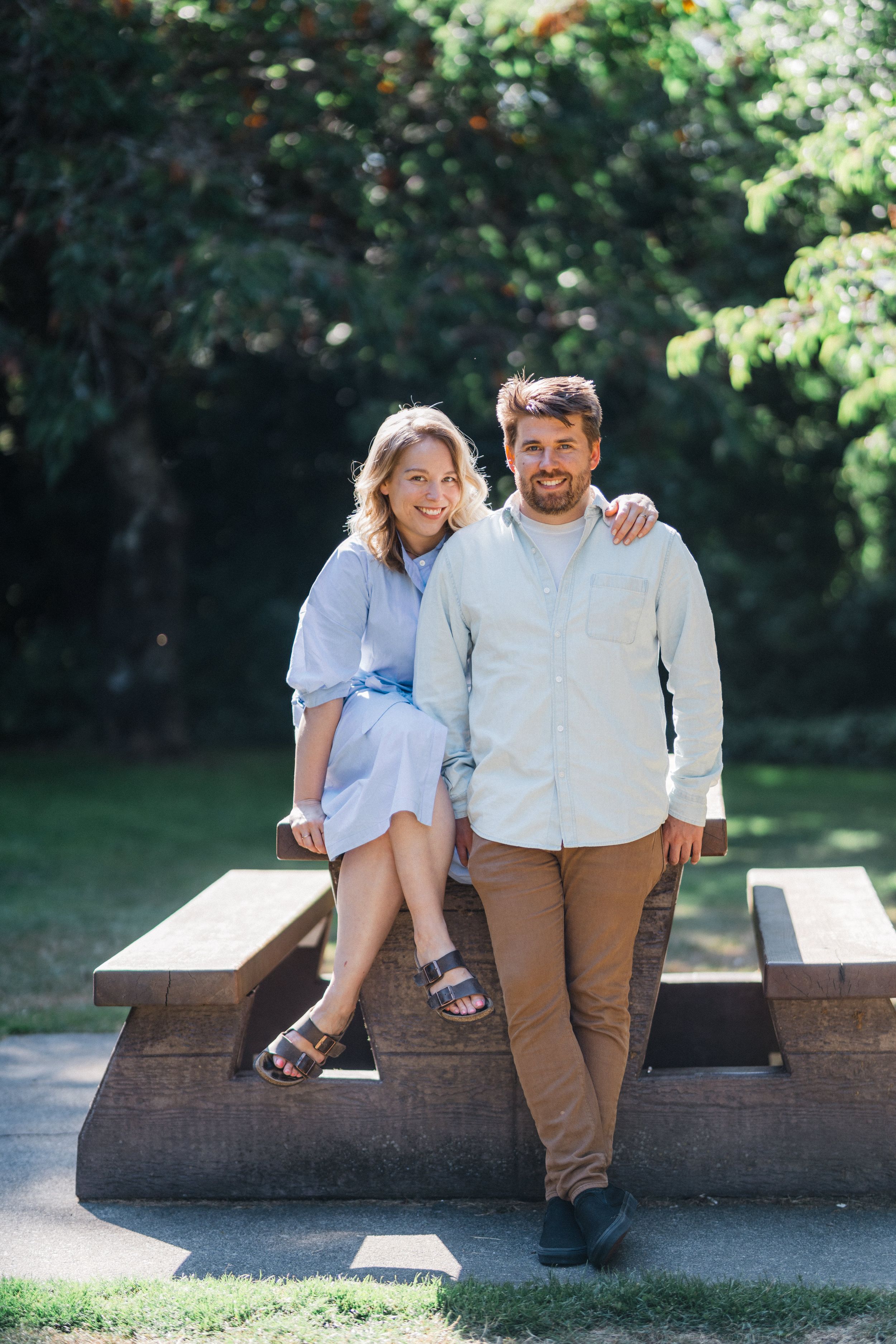 Casual outdoor portrait of couple on wooden bench in sunny garden setting.