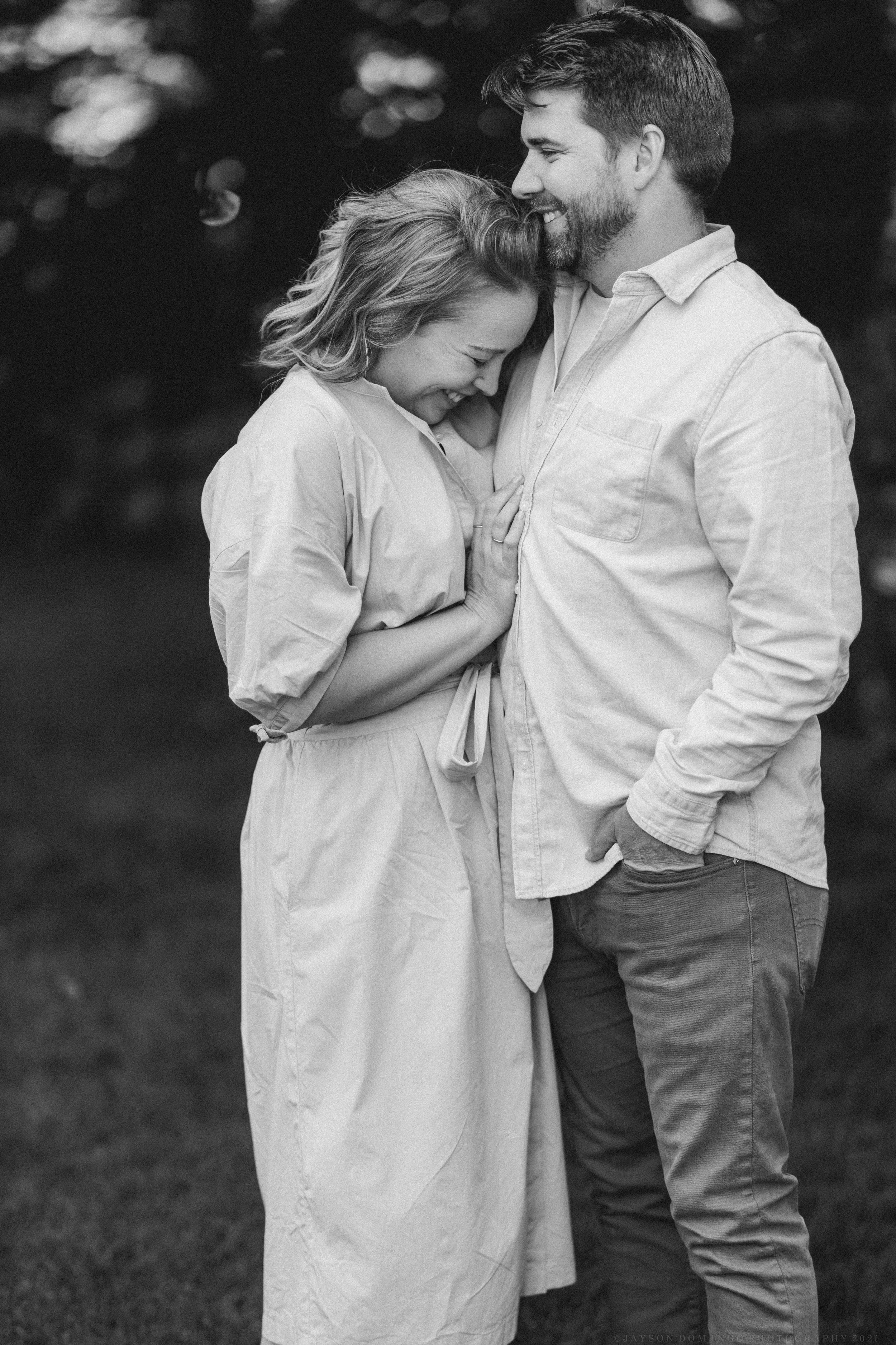Black and white portrait of two people embracing while wearing white clothing outdoors.
