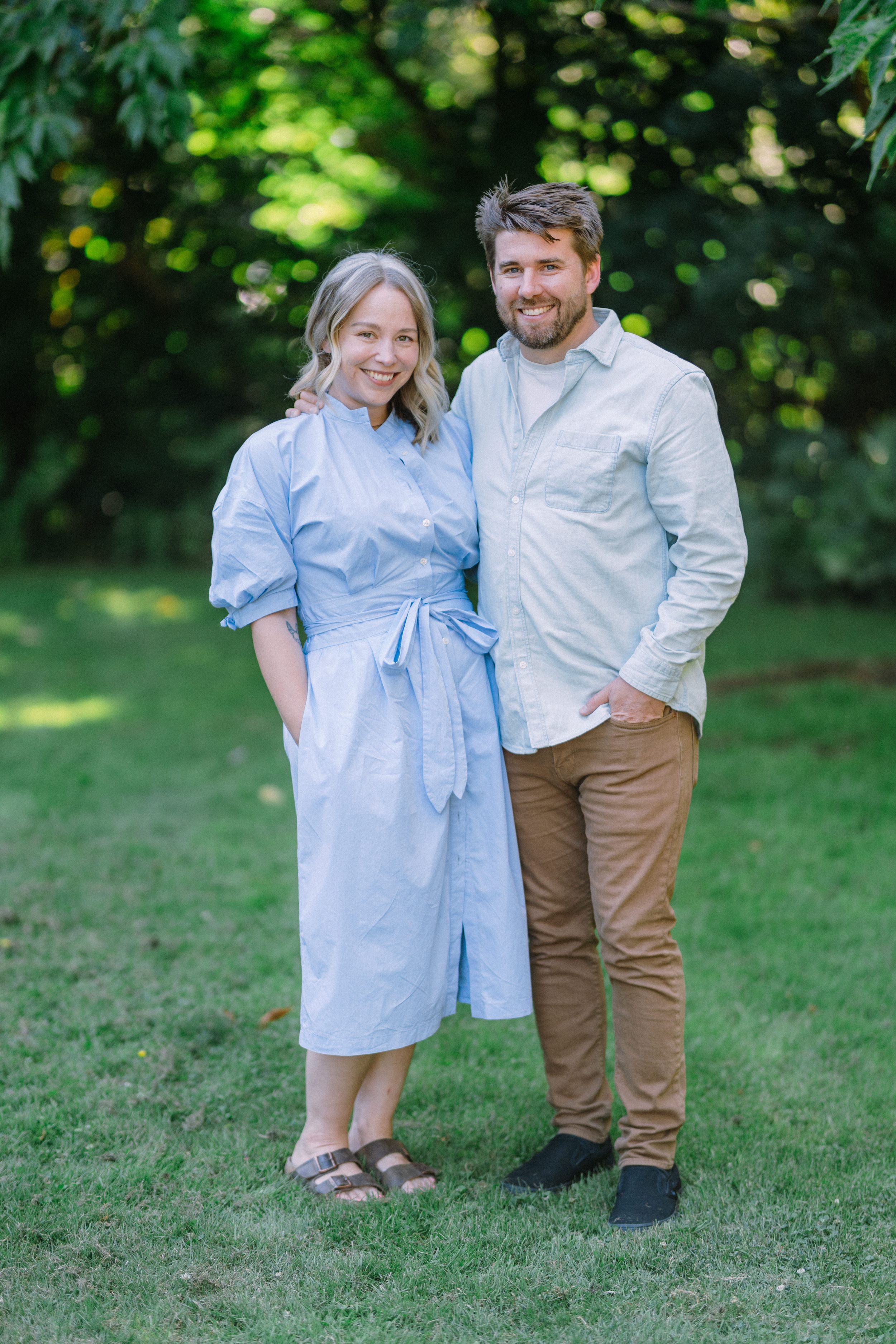 Couple in blue dress and khakis pose together on green grass during summer photoshoot.