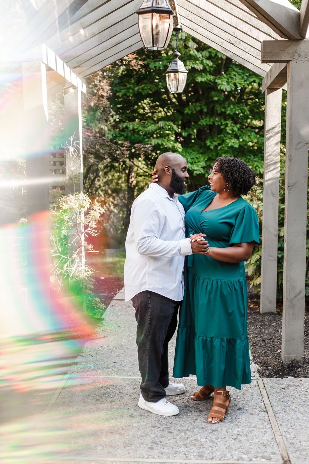 A romantic couple shares an intimate moment under a white pergola with lanterns and greenery.
