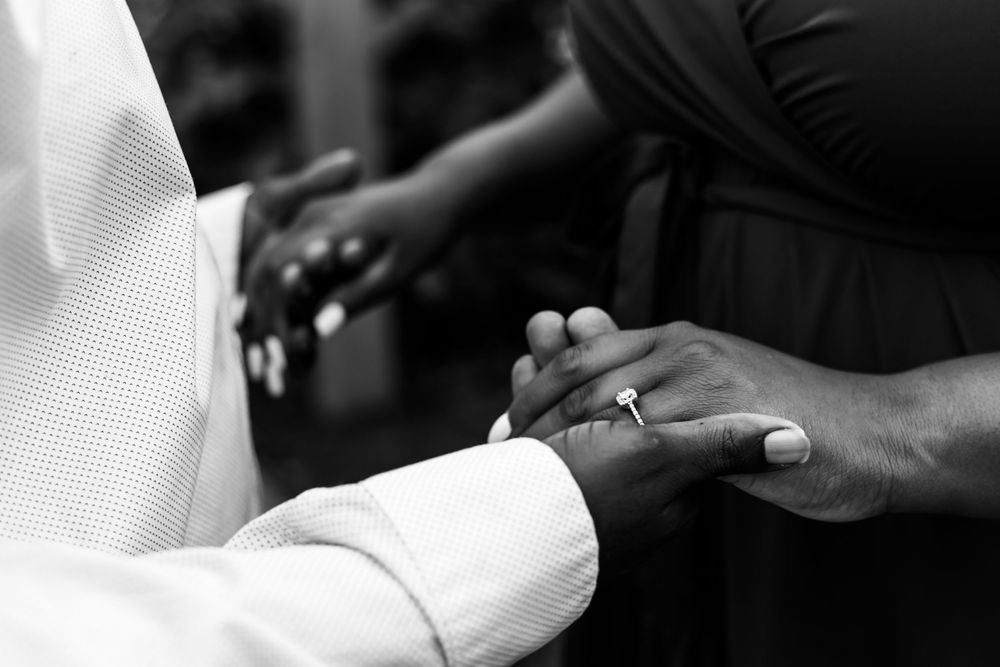 Black and white close-up of hands exchanging wedding rings during a marriage ceremony.