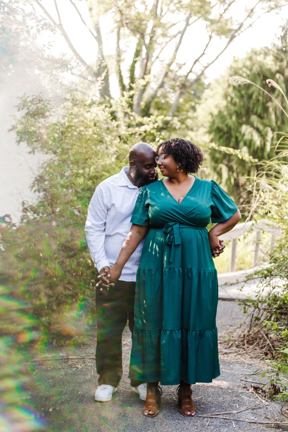 A couple shares a tender moment while walking on a garden path, with the person in a flowing emerald green dress.