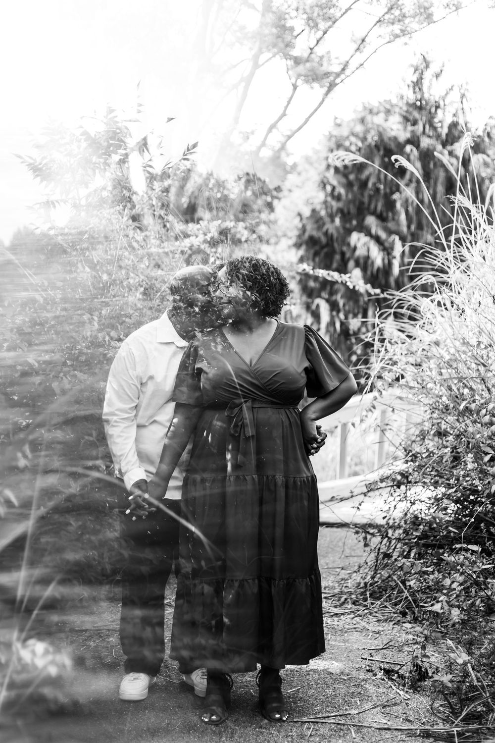 A romantic black and white portrait of two people sharing an intimate moment in a garden setting.
