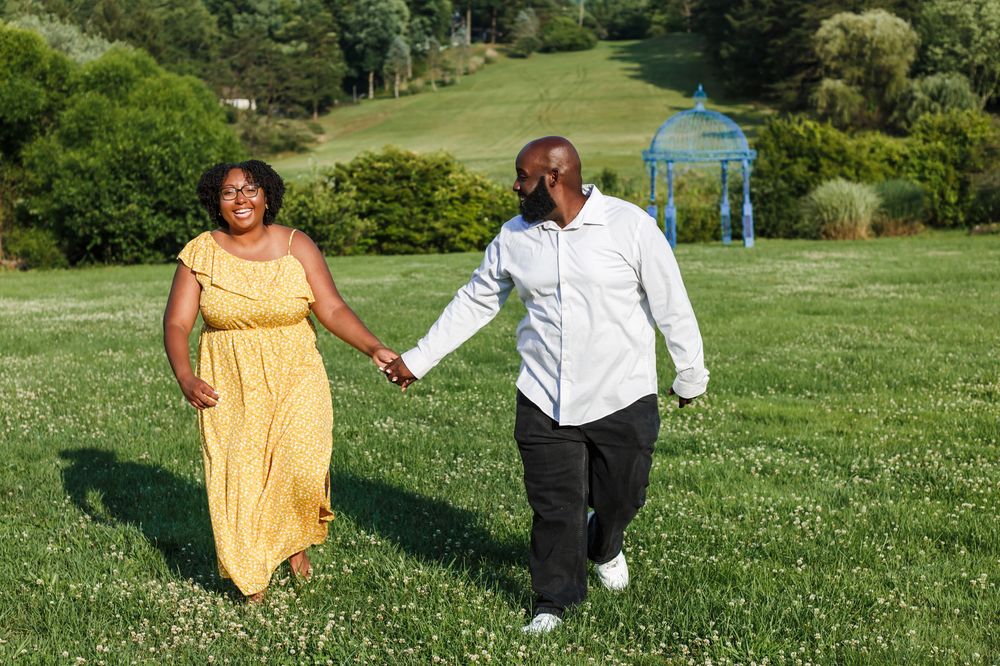 A couple holds hands while walking through a lush green park, with one wearing a flowing yellow dress.