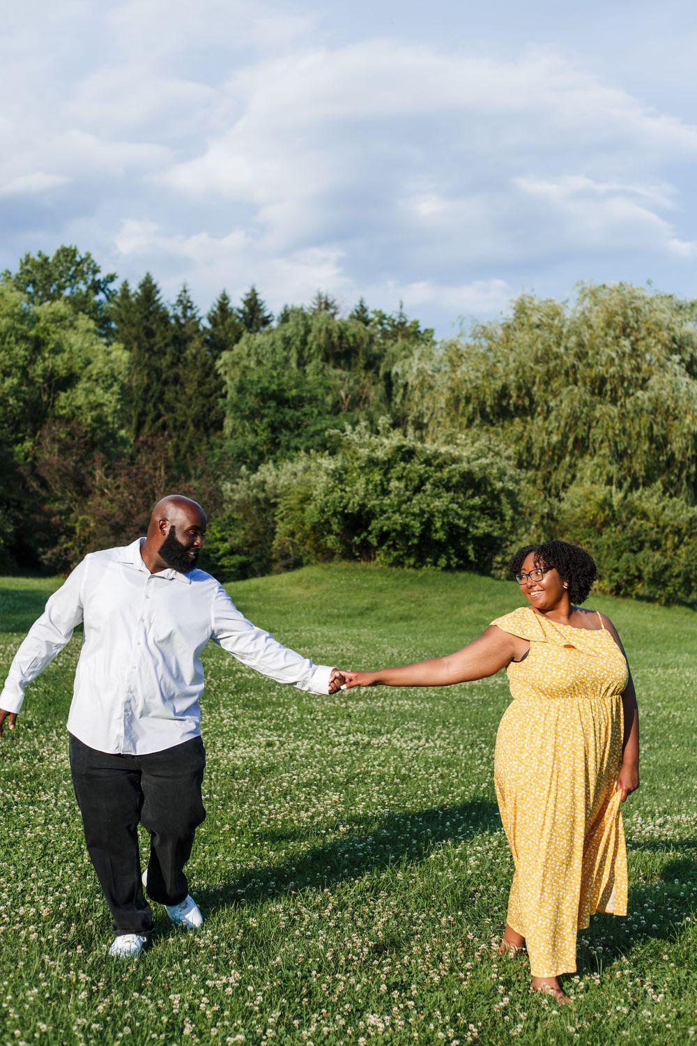 Playful candid sequence of a couple dancing in a sunny meadow with yellow wildflowers and trees in the background.