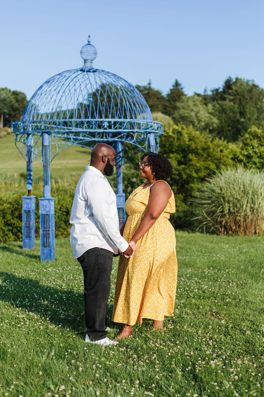 A couple stands together under a decorative blue gazebo in a garden setting.