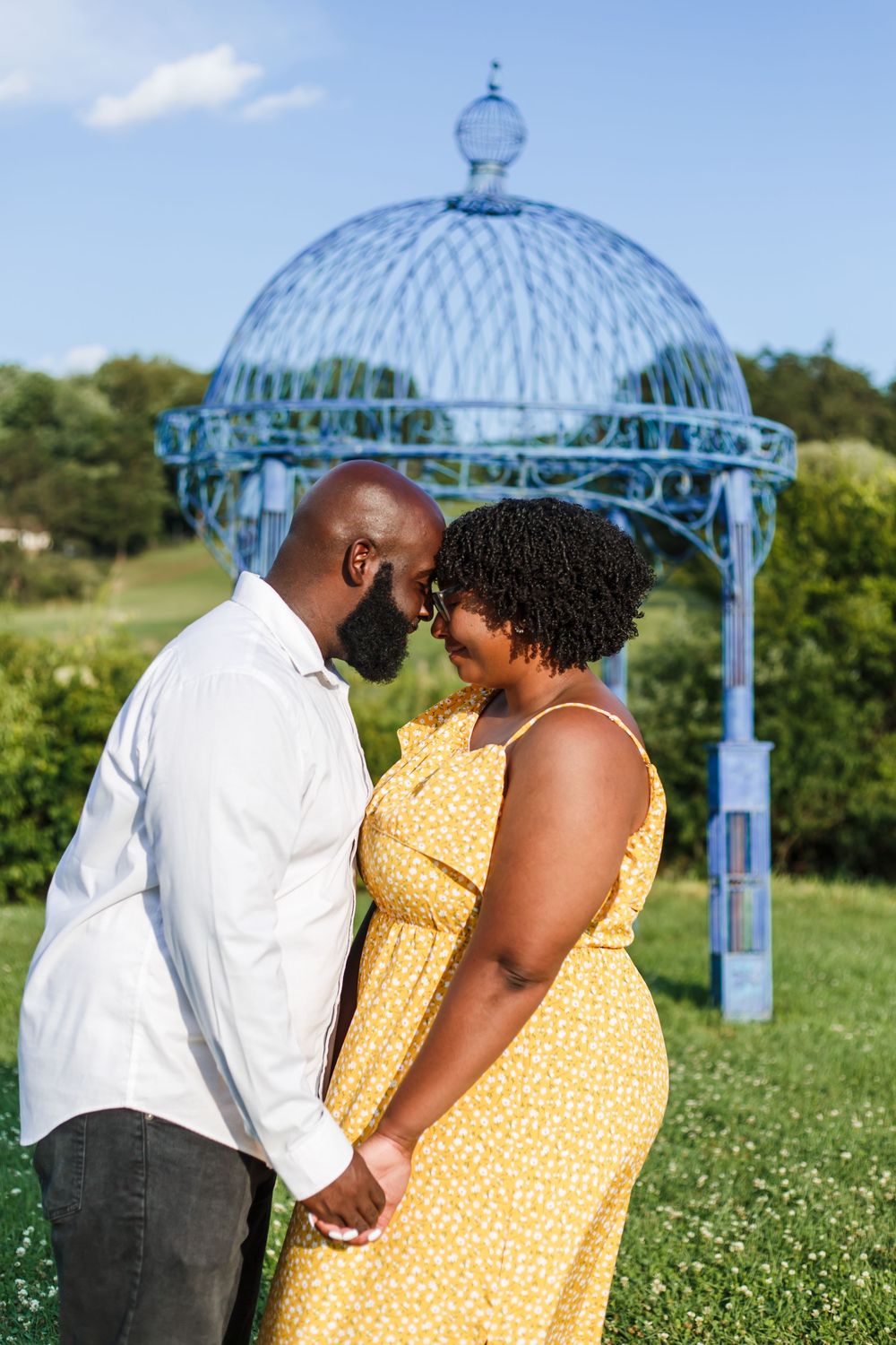 Couple holding hands under a blue metal gazebo in a sunny garden setting.
