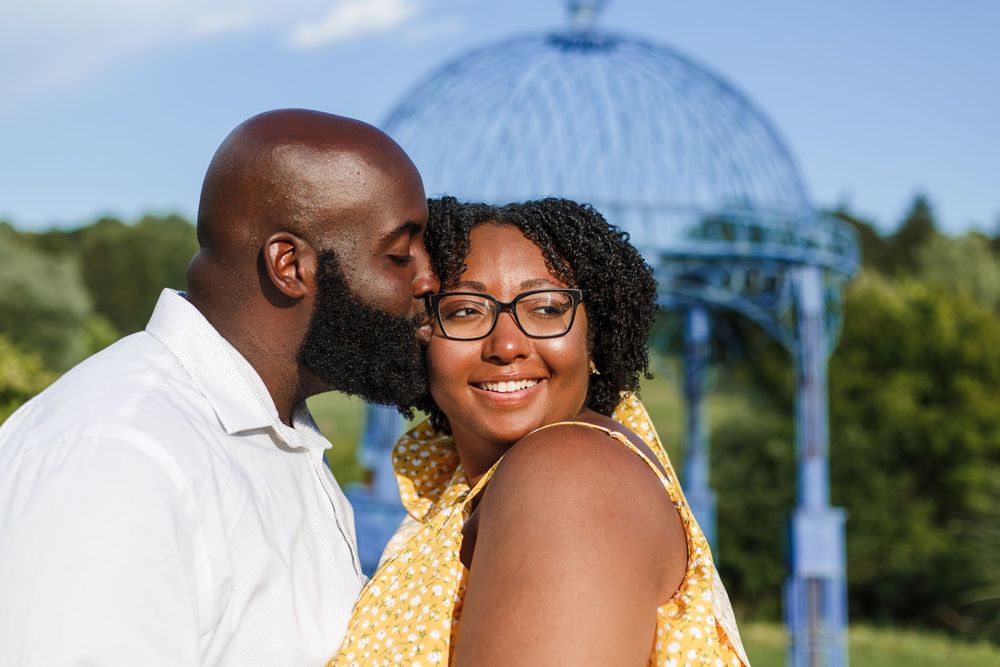 Couple sharing a tender moment under a blue gazebo on a sunny summer day.