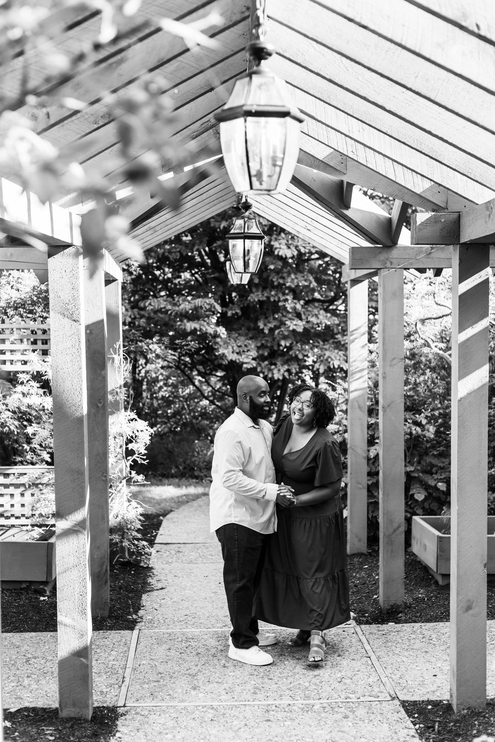 Romantic couple shares intimate moment under white pergola with lanterns in black and white photography.