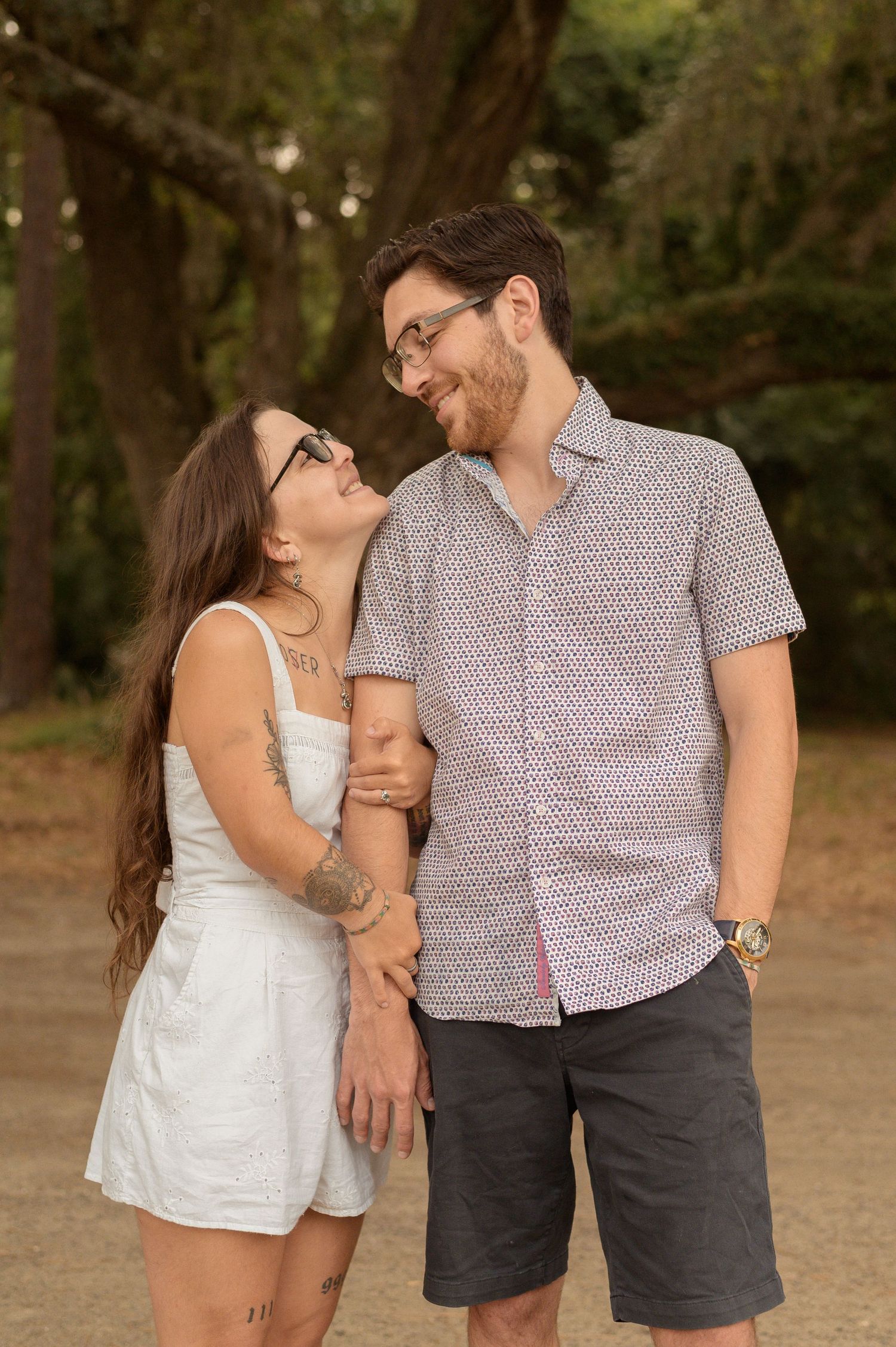 A couple in casual summer attire shares tender moments while walking together in a park setting during golden hour.
