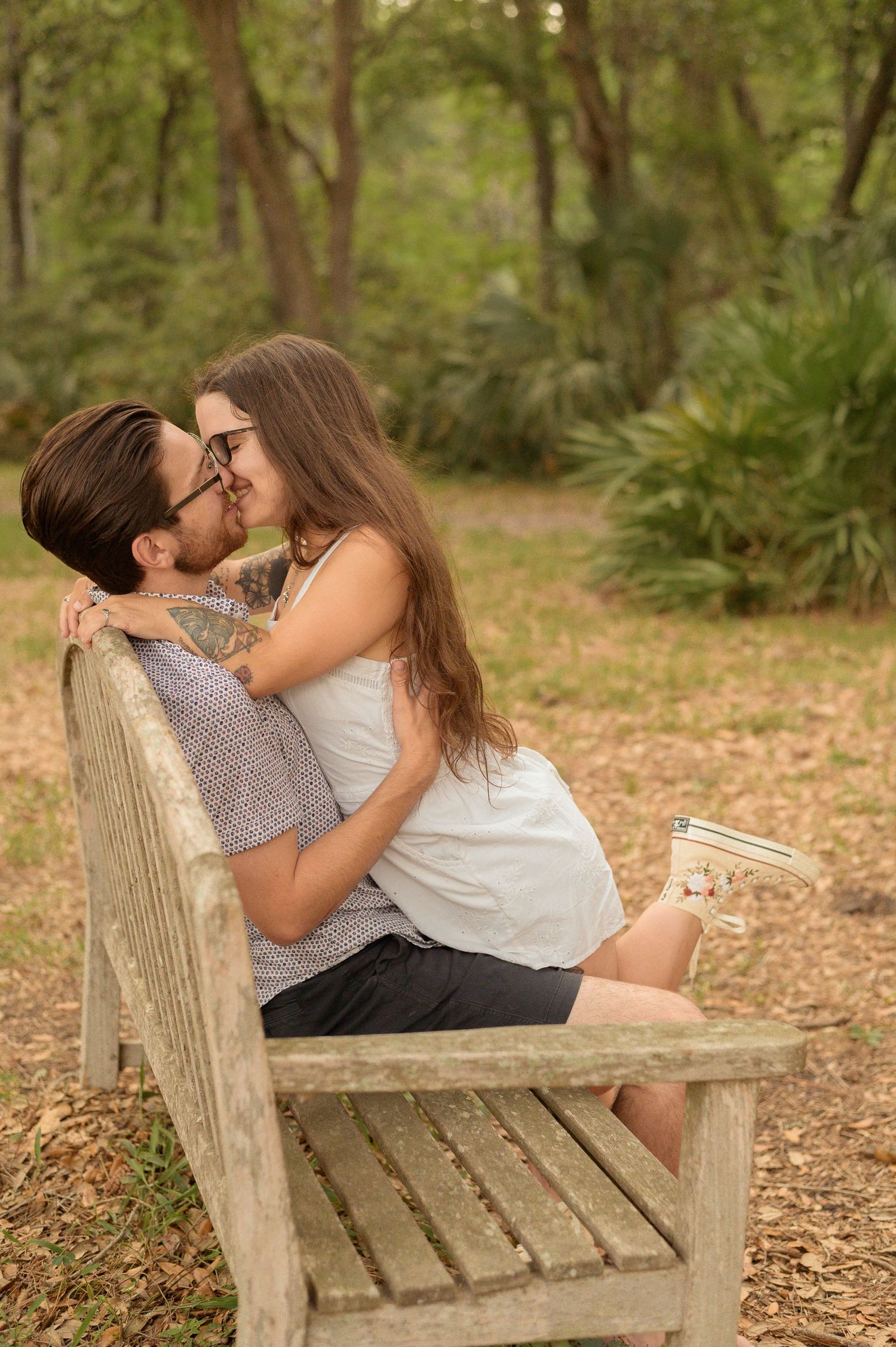 A romantic couple sharing an intimate moment while sitting on a wooden bench in a lush green forest setting.