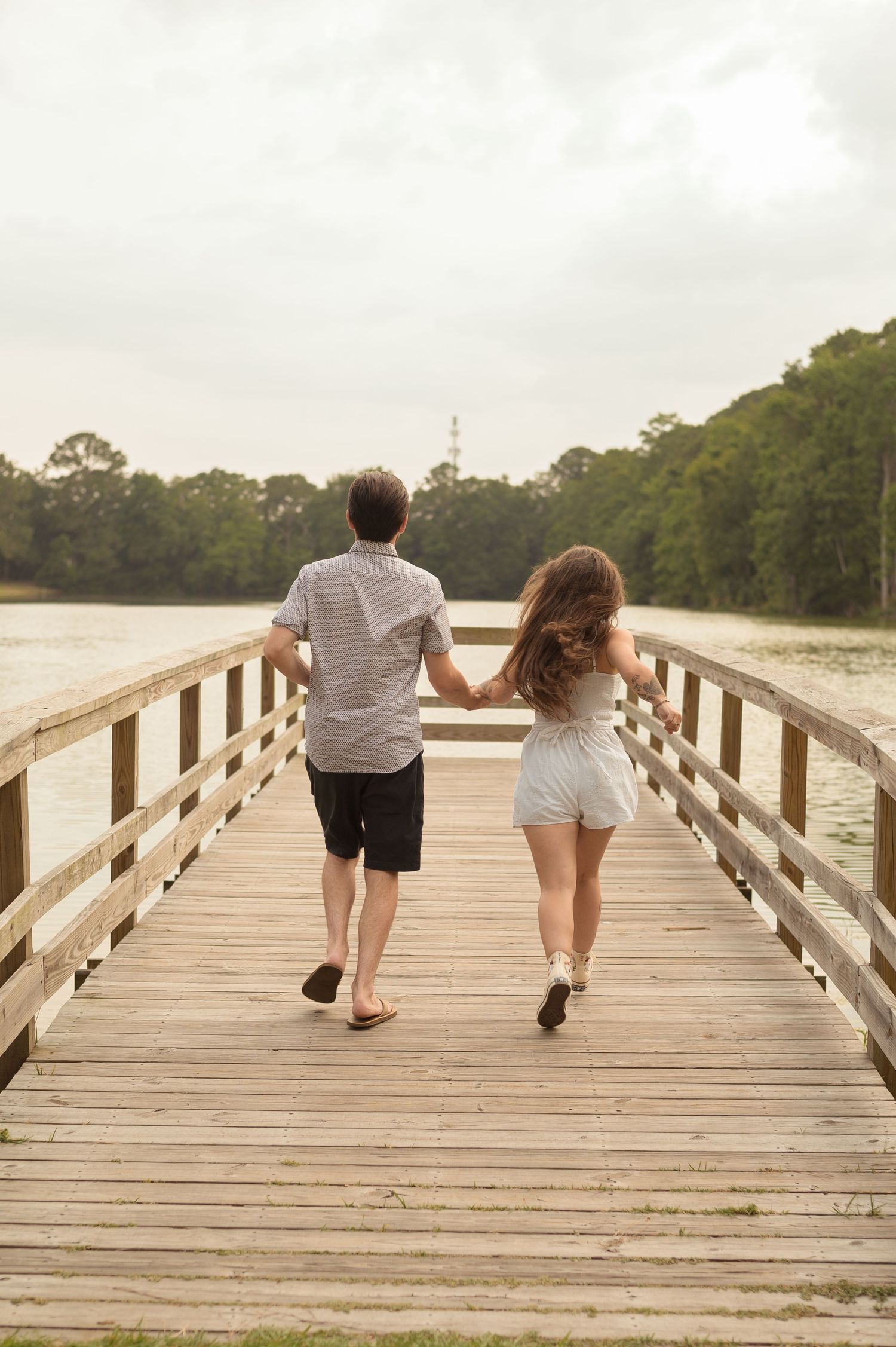 A couple walks together down a wooden boardwalk over a coastal marsh at sunset.