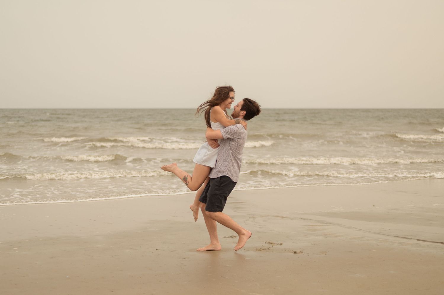 A couple plays and dances together in the ocean waves at the beach.