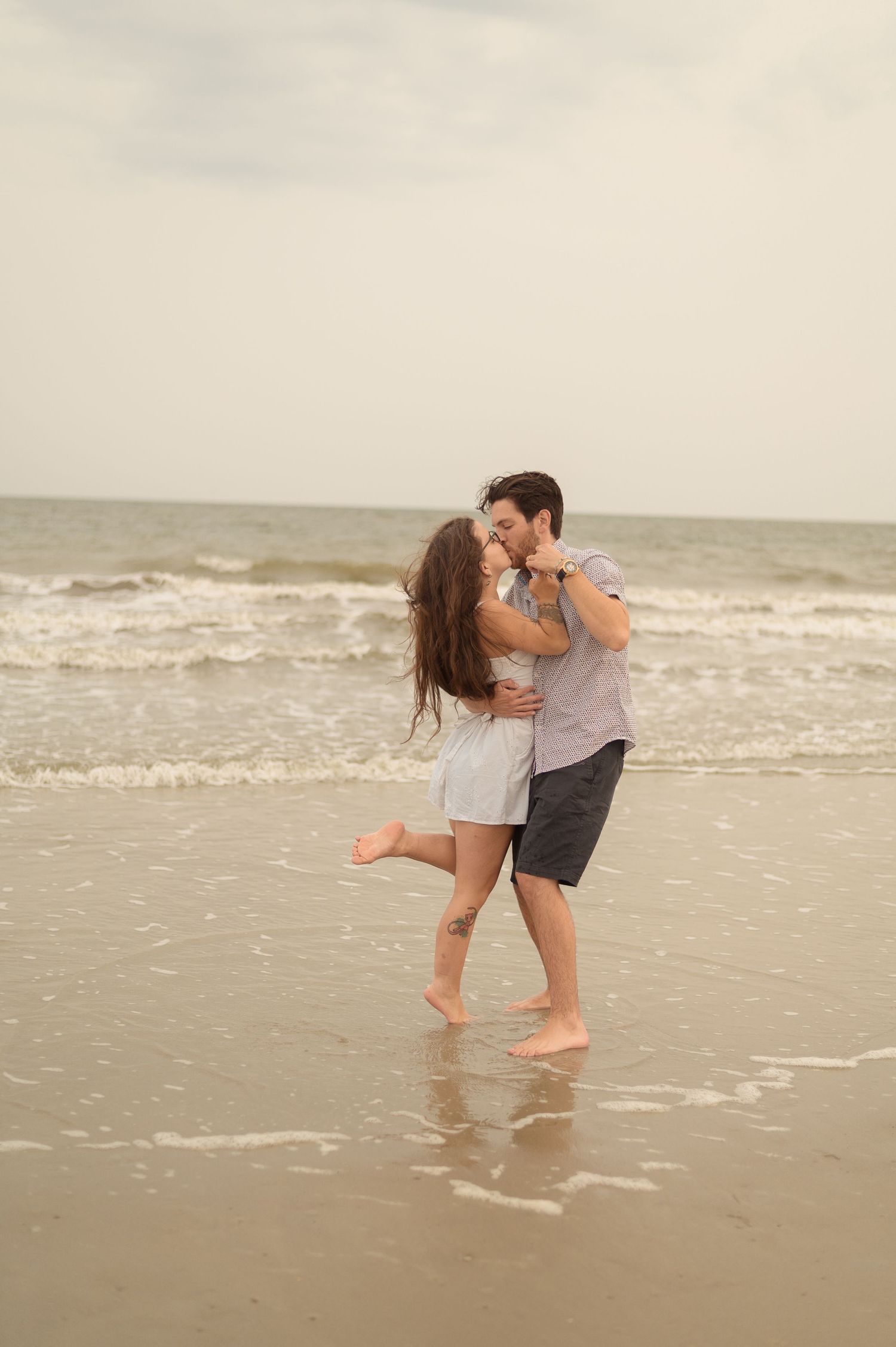 A romantic couple embraces while standing in the shallow ocean water at the beach.