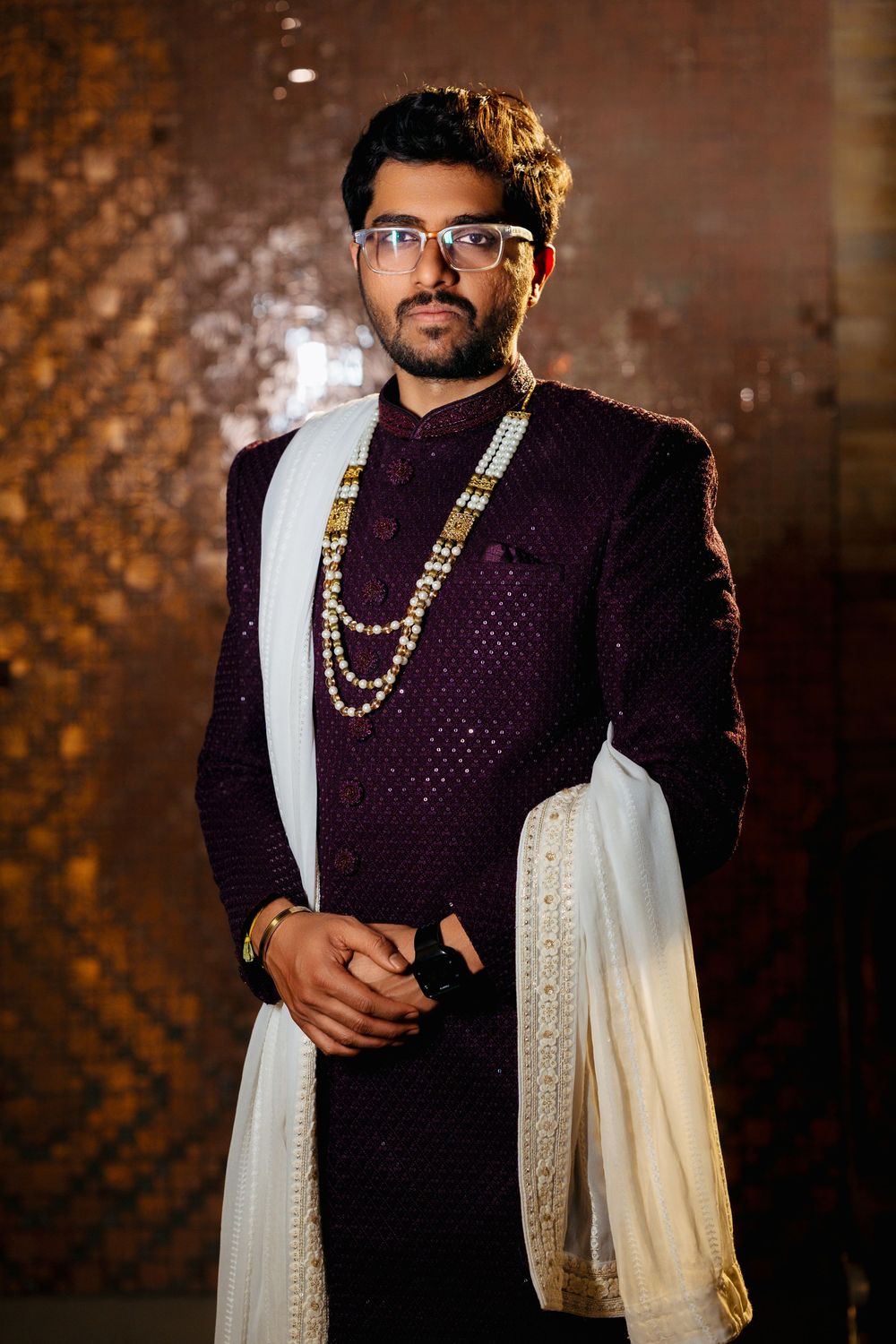 Elegant Indian formal wear featuring a deep purple sherwani with white drape and layered gold necklaces.