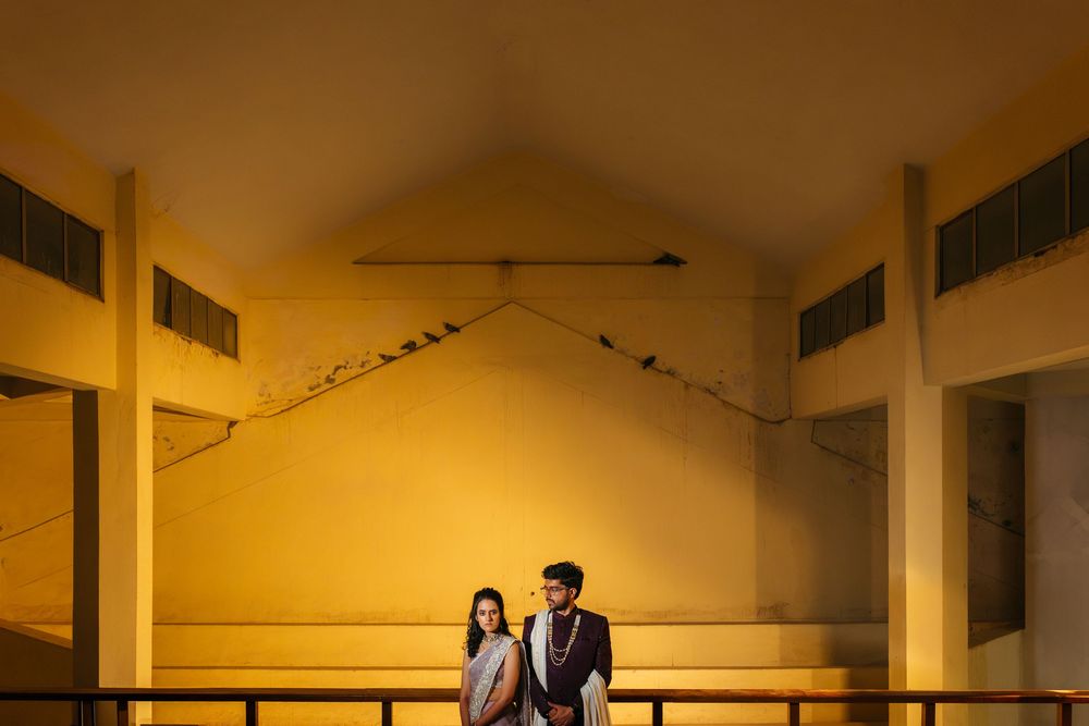 Romantic couple stand in silhouette against warm yellow wall in traditional Indian wedding attire.