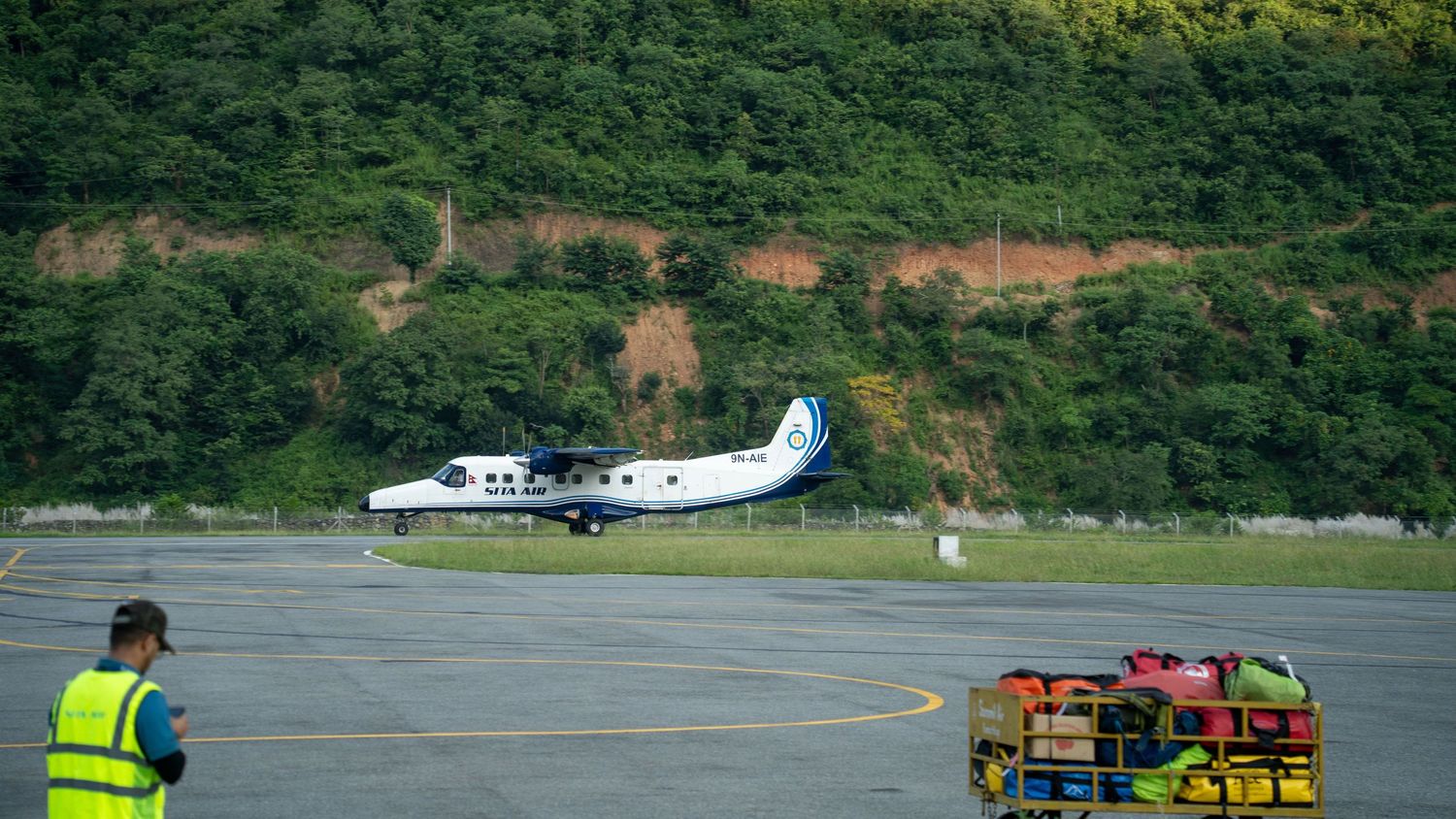 Small aircraft parked on runway with lush green mountains in background.