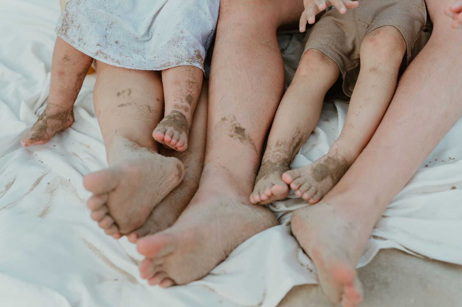 Close-up of muddy feet of adults and children resting on a white blanket at the beach.