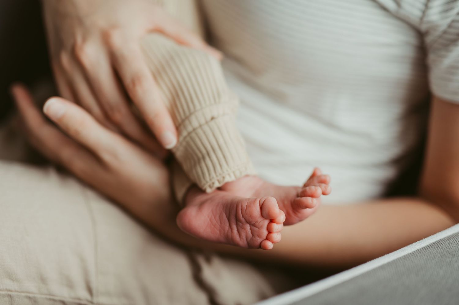 Close-up of a newborn baby's tiny feet resting on a parent's lap in a soft, warm setting.