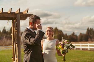 Wedding couple sharing an intimate moment under a wooden arbor during an outdoor countryside ceremony at sunset.