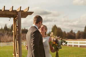A couple shares an intimate moment at a rustic outdoor wedding ceremony under a wooden pergola during golden hour.