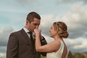 A romantic moment between newlyweds sharing a tender gesture under a cloudy sky at sunset.