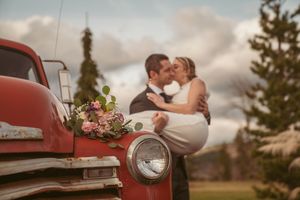 Vintage red pickup truck adorns a rustic outdoor scene with bridal bouquet of pink flowers in a romantic wedding setting.