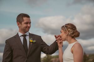 A romantic outdoor wedding moment captured at sunset with the couple sharing a tender gesture under cloudy skies.