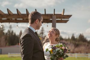 A happy couple shares a joyful moment outdoors at their wedding celebration with a wooden pergola in the background.