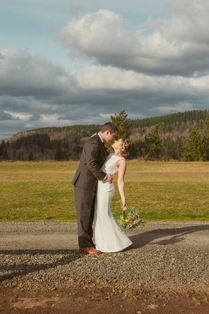 Wedding couple sharing romantic moment in rural field setting with mountains and dramatic sky backdrop.
