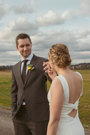 A couple shares a candid wedding moment outdoors with dramatic clouds and rolling hills in background.