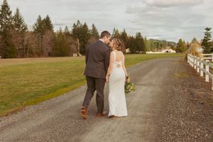 A couple walking down a gravel road with rustic fencing and evergreen trees in the background.